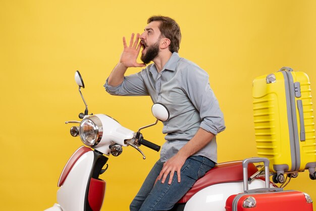 Vue de face du concept de voyage avec jeune homme assis sur une moto avec des valises sur elle appelant quelqu'un sur jaune