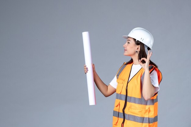 Vue de face du constructeur féminin avec une affiche dans ses mains sur un mur gris