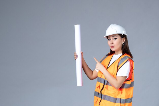 Vue de face du constructeur féminin avec une affiche dans ses mains sur un mur gris