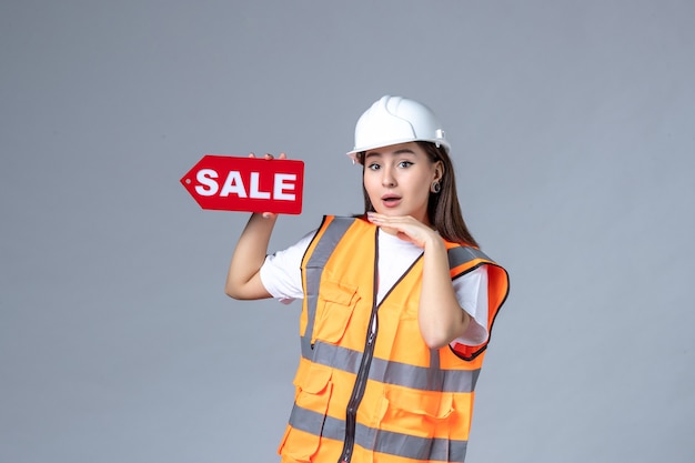 Vue de face du constructeur féminin tenant un tableau de vente rouge sur un mur blanc
