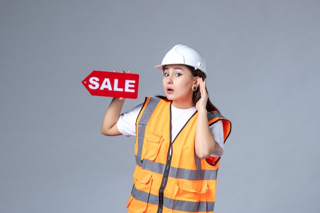 Vue de face du constructeur féminin tenant un tableau de vente rouge sur un mur blanc