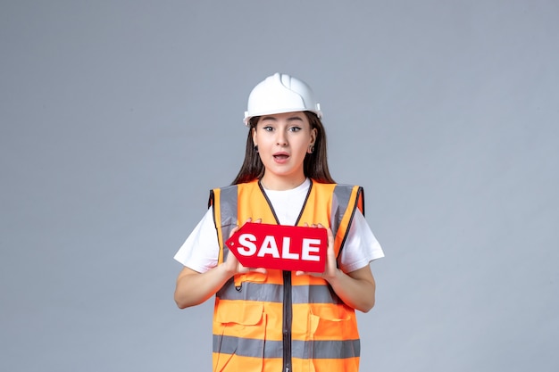 Vue de face du constructeur féminin tenant un tableau de vente rouge sur un mur blanc