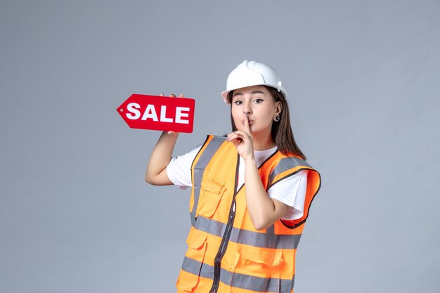 Vue de face du constructeur féminin tenant un tableau de vente rouge sur un mur blanc