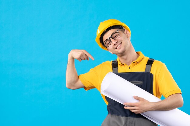 Vue de face du constructeur masculin en uniforme jaune et casque avec plan sur mur bleu