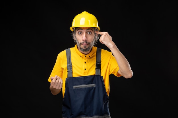 Vue de face du constructeur masculin en uniforme sur le mur noir