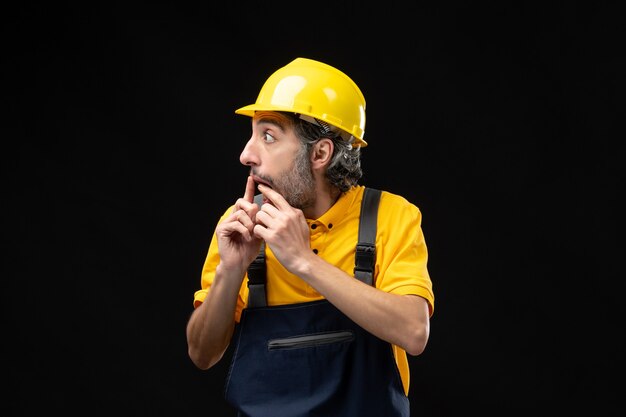 Vue de face du constructeur masculin en uniforme sur le mur noir