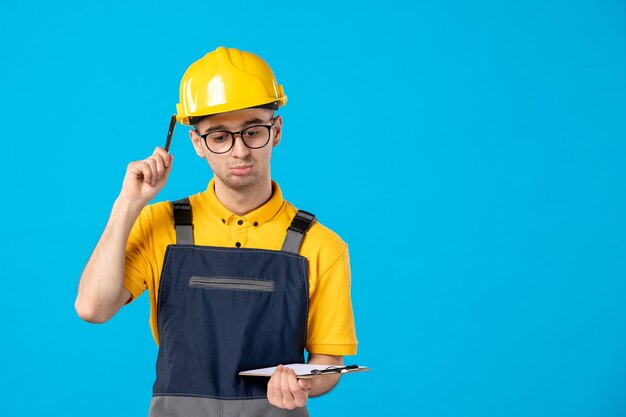 Vue de face du constructeur masculin en uniforme avec note de fichier dans ses mains sur le mur bleu