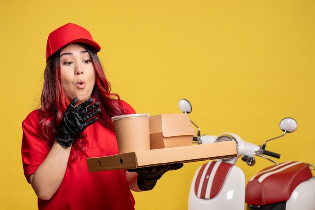 Vue de face du courrier féminin avec livraison de nourriture et de dessert sur mur jaune