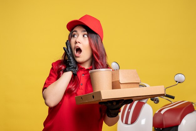 Vue de face du courrier féminin avec livraison de nourriture et de dessert sur mur jaune