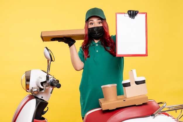 Vue de face du courrier féminin en masque avec livraison de café et de nourriture sur mur jaune