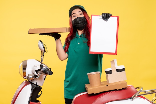 Vue de face du courrier féminin en masque avec livraison de café et de nourriture sur mur jaune