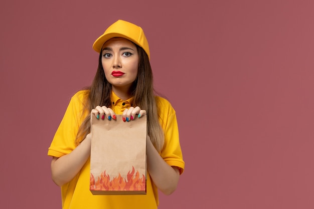 Vue de face du courrier féminin en uniforme jaune et cap tenant le paquet alimentaire sur le mur rose clair