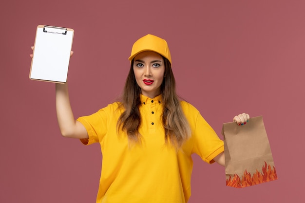 Vue de face du courrier féminin en uniforme jaune et cap tenant le paquet de nourriture et le bloc-notes sur le mur rose