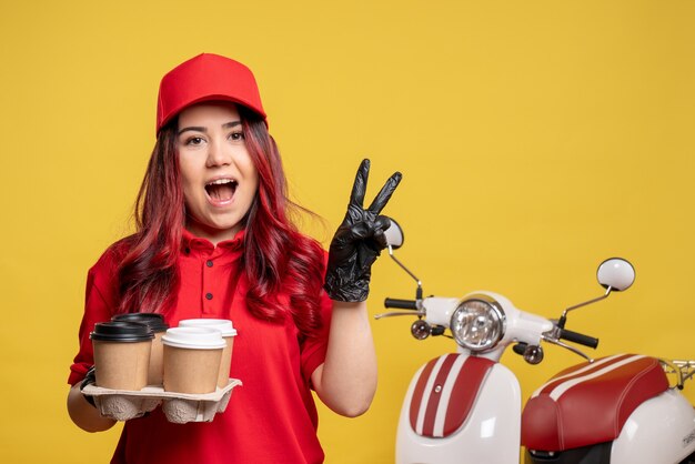 Vue de face du courrier féminin en uniforme rouge avec du café sur le mur jaune