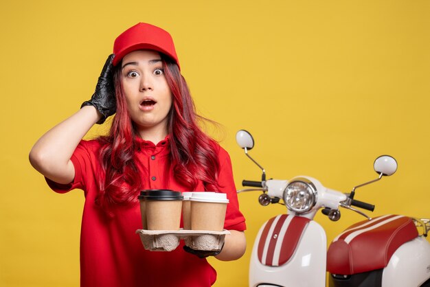 Vue de face du courrier féminin en uniforme rouge avec du café sur le mur jaune