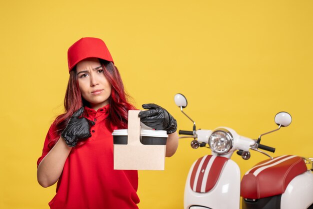 Vue de face du courrier féminin en uniforme rouge avec du café sur le mur jaune