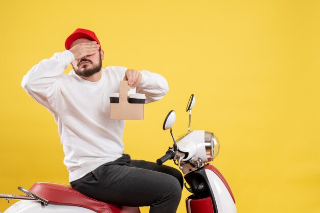 Vue de face du courrier masculin tenant le café de livraison couvrant ses yeux sur le mur jaune