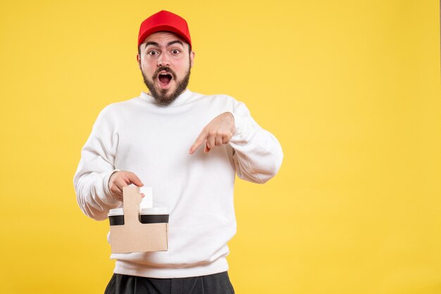 Vue de face du courrier masculin tenant le café de livraison sur le mur jaune