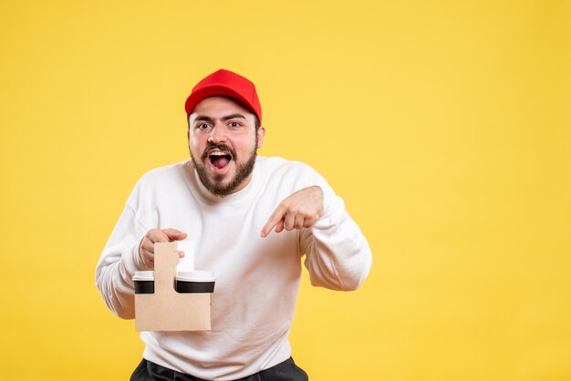 Vue de face du courrier masculin tenant le café de livraison sur le mur jaune