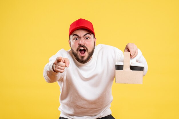 Vue de face du courrier masculin tenant le café de livraison sur le mur jaune