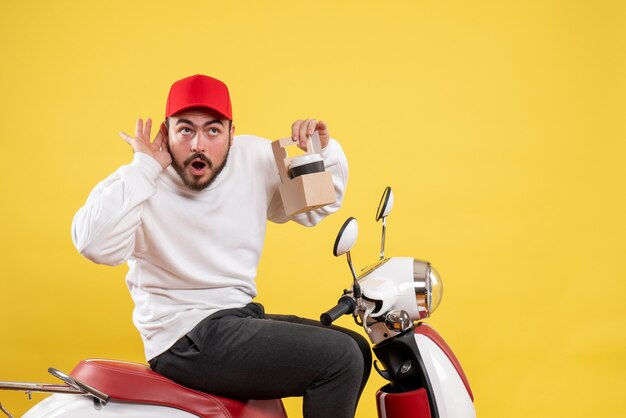 Vue de face du courrier masculin tenant le café de livraison sur le mur jaune