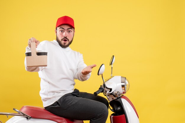 Vue de face du courrier masculin tenant le café de livraison sur le mur jaune