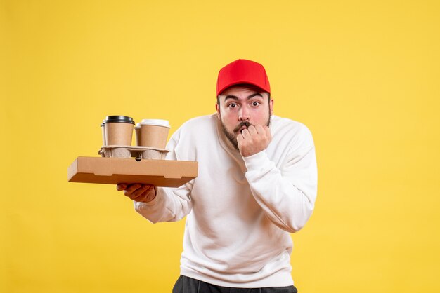 Vue de face du courrier masculin tenant la livraison de nourriture et de café sur le mur jaune