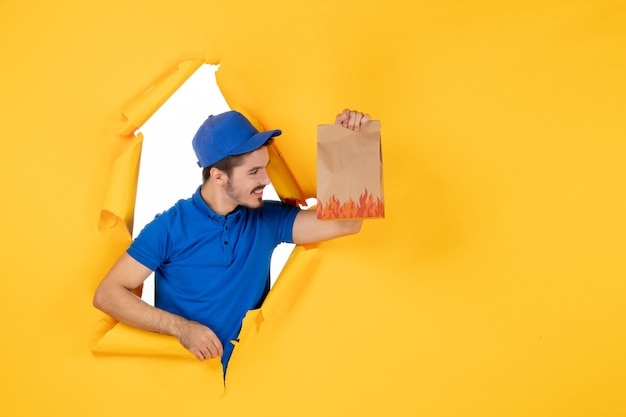 Photo gratuite vue de face du courrier masculin en uniforme bleu tenant un emballage de nourriture sur un espace jaune