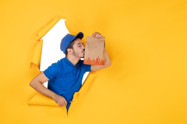 Vue de face du courrier masculin en uniforme bleu tenant un emballage de nourriture sur un espace jaune