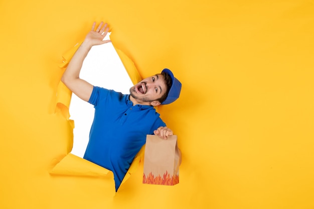 Vue de face du courrier masculin en uniforme bleu tenant un emballage de nourriture sur un espace jaune