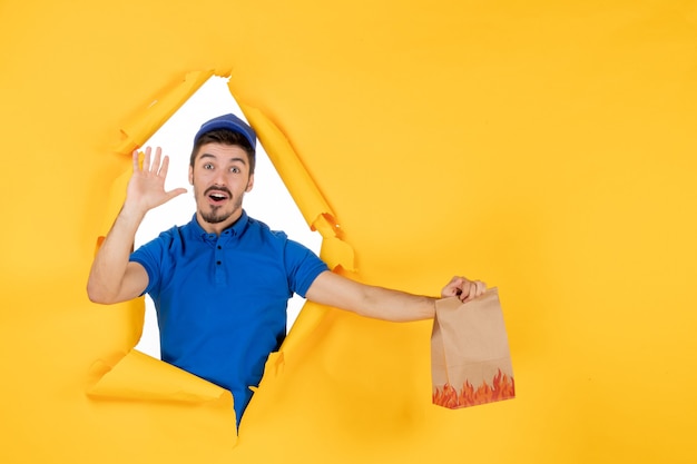 Vue de face du courrier masculin en uniforme bleu tenant un emballage de nourriture sur un espace jaune