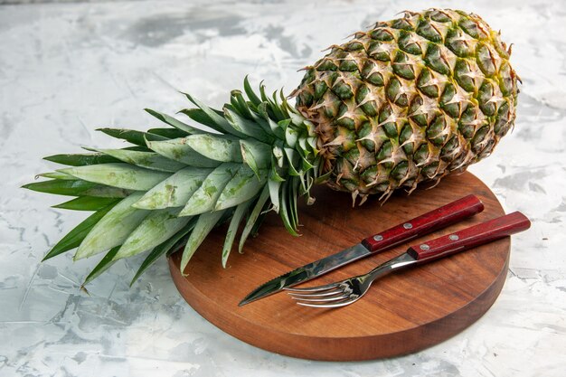 Vue de face du couteau fourchette d'ananas doré frais entier sur une planche à découper sur une surface en marbre