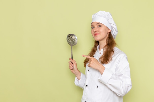 Vue de face du cuisinier portant un costume de cuisinier blanc tenant une grande cuillère en argent sur le mur vert