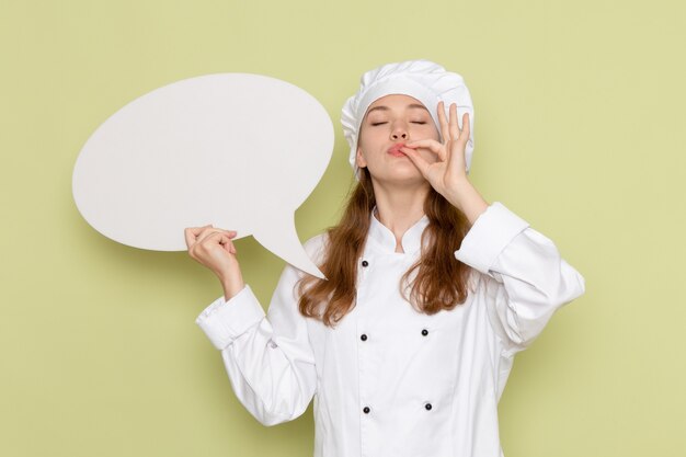 Vue de face du cuisinier portant un costume de cuisinier blanc tenant une grande pancarte blanche sur le mur vert