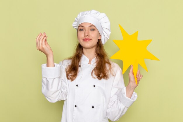 Vue de face du cuisinier portant un costume de cuisinier blanc tenant un panneau jaune sur le mur vert