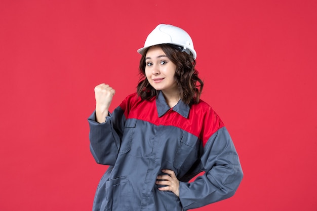 Vue de face du fier constructeur féminin en uniforme avec un casque sur fond rouge isolé