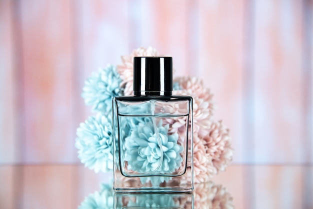 Photo gratuite vue de face du flacon de parfum devant des fleurs sur beige floue