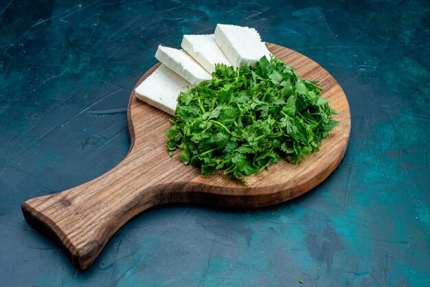 Vue de face du fromage blanc avec des verts frais sur le fond bleu foncé.