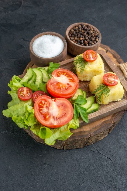 Vue de face du fromage de légumes frais hachés et entiers sur une planche à découper et des épices sur une surface noire