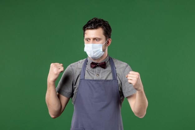 Vue de face du garçon pensant en uniforme avec masque médical sur mur vert