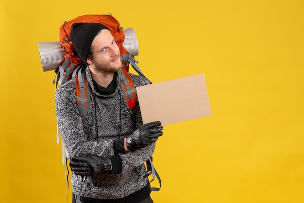 Photo gratuite vue de face du jeune auto-stoppeur heureux avec des gants en cuir et sac à dos tenant un carton vierge