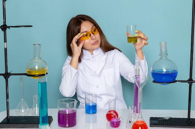 Vue de face du jeune chimiste en costume blanc en face de table travaillant avec des solutions