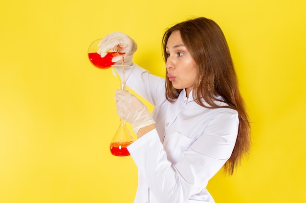 Vue de face du jeune chimiste féminin en costume blanc travaillant avec des solutions chimiques