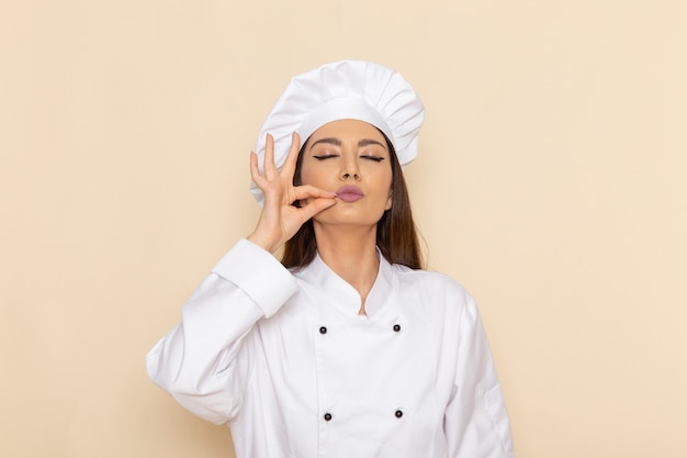 Vue de face du jeune cuisinier en costume de cuisinier blanc montrant un délicieux signe sur un mur blanc clair