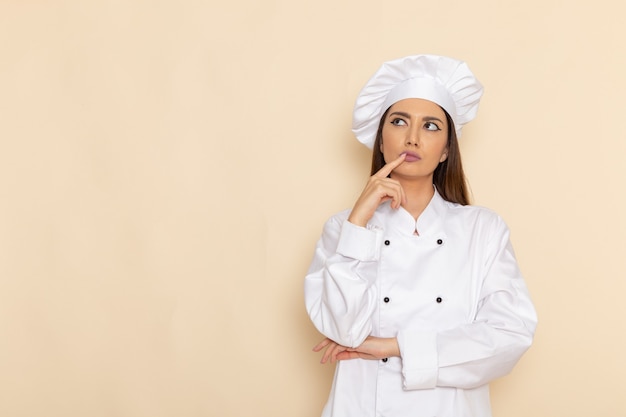 Vue de face du jeune cuisinier en costume de cuisinier blanc pensant juste sur un mur blanc clair