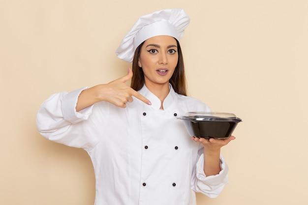 Vue de face du jeune cuisinier en costume de cuisinier blanc tenant un bol sombre sur un mur blanc