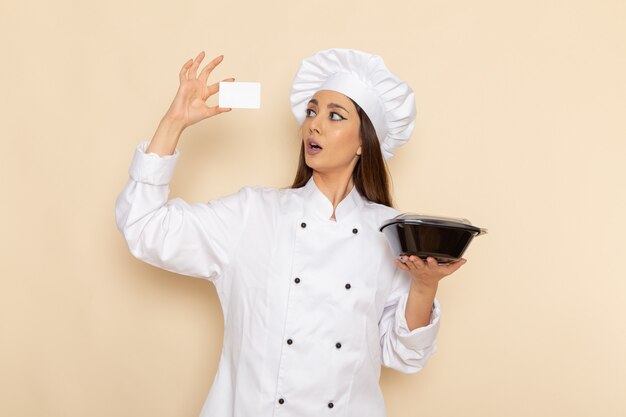 Vue de face du jeune cuisinier en costume de cuisinier blanc tenant la casserole sur le mur blanc