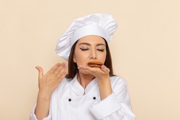 Vue de face du jeune cuisinier en costume de cuisinier blanc tenant des cookies sur un mur blanc clair