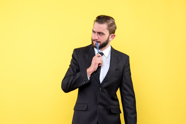 Vue de face du jeune homme d'affaires ayant une idée de mettre un crayon sur la bouche jaune