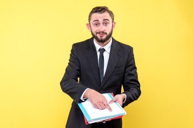 Vue de face du jeune homme d'affaires avec un sourire pointe avec optimisme avec un doigt vers les documents sur jaune